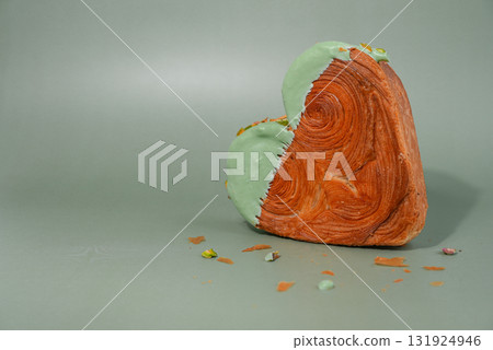 Heart shaped pistachio croissant on green background with copy space. Puff pastry trendy sweet dessert bakery. Creamy dough experiment Heart shaped pistachio croissant on green background with copy space. Puff pastry trendy sweet dessert bakery. Creamy dough experiment 131924946