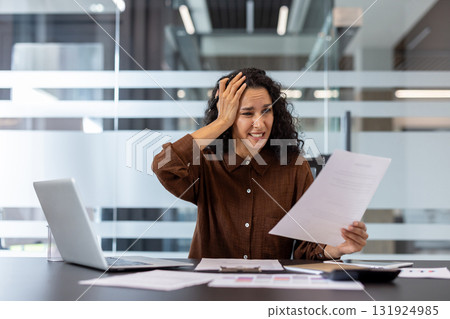 Stressed businesswoman holding a document and clutching her head, experiencing frustration and anxiety from work problems and overwhelming paperwork in her office cubicle Stressed businesswoman holding a document and clutching her head, experiencing frustration and anxiety from work problems and overwhelming paperwork in her office cubicle 131924985