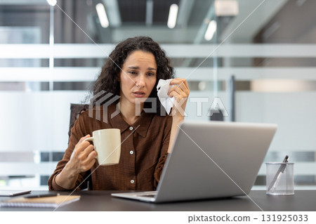 Young woman working on a laptop, wiping tears with a tissue, conveying emotional distress and showing symptoms of burnout from overwhelming work pressure in a modern office environment Young woman working on a laptop, wiping tears with a tissue, conveying emotional distress and showing symptoms of burnout from overwhelming work pressure in a modern office environment 131925033