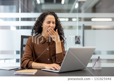 Businesswoman yawning and covering her mouth at a modern office desk, tired and overworked while working on a laptop, showing burnout, fatigue and low energy during long hours Businesswoman yawning and covering her mouth at a modern office desk, tired and overworked while working on a laptop, showing burnout, fatigue and low energy during long hours 131925048