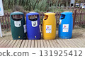 Colorful waste bins arranged in a row on a wooden walkway, promoting recycling and waste management, surrounded by greenery and a clean environment 131925412
