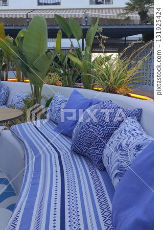 Cozy outdoor seating area featuring blue patterned cushions and lush greenery, creating a serene atmosphere for relaxation and social gatherings in a stylish environment 131925424