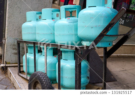 A cart loaded with multiple turquoise propane tanks, ready for delivery or service, placed on a city street. They are stacked neatly. 131925517