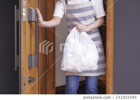 A woman in an apron taking out household garbage A woman in an apron taking out household garbage 131925593