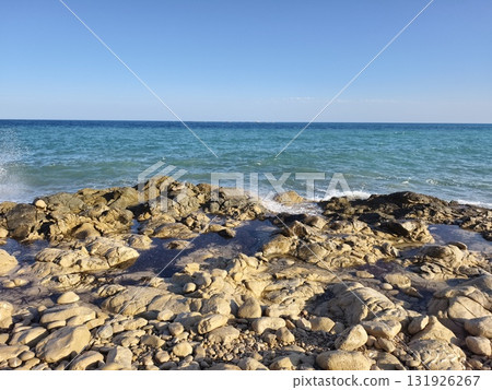 A serene coastal landscape showcases the clear blue ocean alongside a rugged rocky shoreline A serene coastal landscape showcases the clear blue ocean alongside a rugged rocky shoreline 131926267