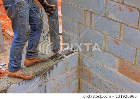 Construction worker fills cinder block wall with concrete using cement pipe pump while working on new building 131926966