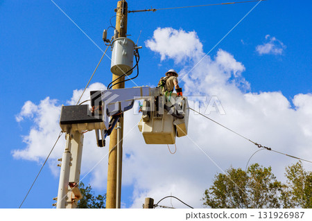 Utility electrical worker in bucket lifts to repair power lines on tall wooden pole under works day 131926987