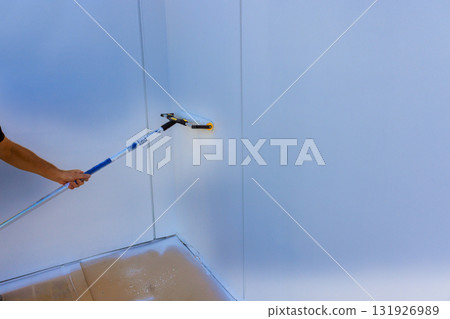 Handyman is using paint roller on wall in bright room, focusing on even coverage. Handyman is using paint roller on wall in bright room, focusing on even coverage. 131926989