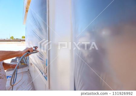 Worker is applying paint to an exterior wall using spray gun while construction area. Worker is applying paint to an exterior wall using spray gun while construction area. 131926992