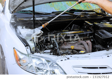 Worker is using pressure washer to clean engine bay of white car at auto service center 131927012