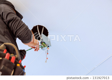 An electrician works on installing new light fixture inside ceiling, focusing on wiring connections. 131927013