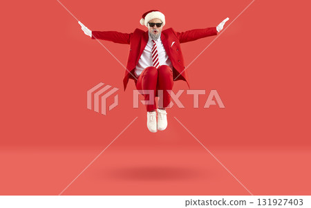 Cool funny man in red formal suit and Santa hat jumping high isolated on red background. Cool funny man in red formal suit and Santa hat jumping high isolated on red background. 131927403