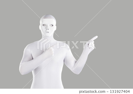 Mysterious man in white mask and spandex bodysuit pointing to side on grey background 131927404