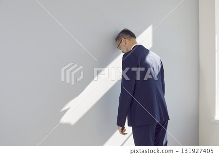 Stressed man gets tired of business problems and bangs his head against office wall 131927405