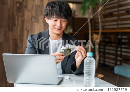 一位商人一邊在咖啡館吃飯團,一邊在電腦上工作 一位商人一邊在咖啡館吃飯團,一邊在電腦上工作 131927759