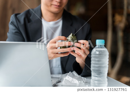 A businessman/man working on a computer while eating rice balls in a cafe A businessman/man working on a computer while eating rice balls in a cafe 131927761