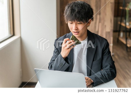 A businessman/man working on a computer while eating rice balls in a cafe A businessman/man working on a computer while eating rice balls in a cafe 131927762