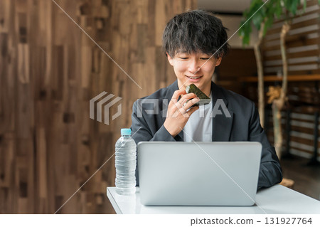 A businessman/man working on a computer while eating rice balls in a cafe 131927764
