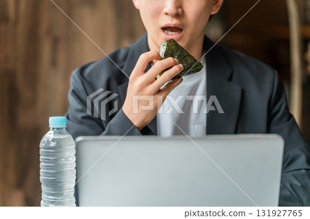 A businessman/man working on a computer while eating rice balls in a cafe A businessman/man working on a computer while eating rice balls in a cafe 131927765