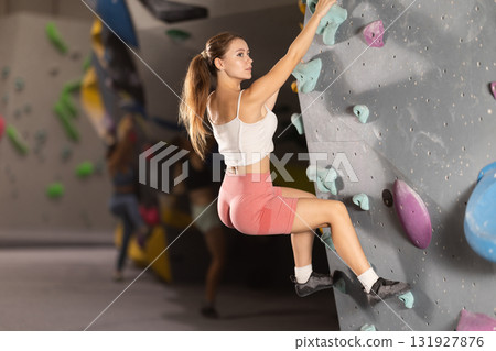 Woman exercising on wall in climbing gym during bouldering training Woman exercising on wall in climbing gym during bouldering training 131927876
