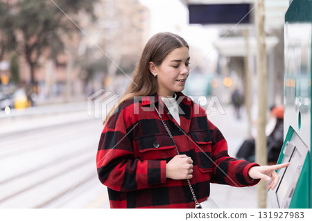Girl buys travel ticket from machine at tramway stop Girl buys travel ticket from machine at tramway stop 131927983