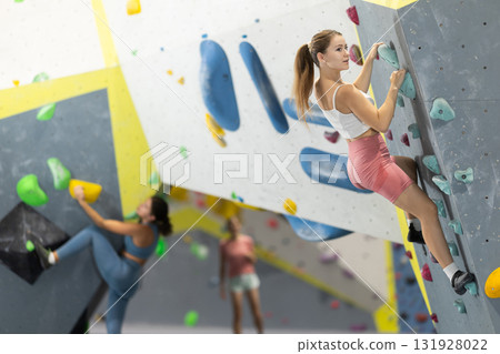 Girl climbs artificial wall bouldering, working out in gym Girl climbs artificial wall bouldering, working out in gym 131928022