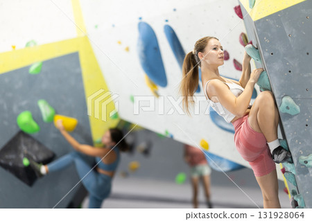 Girl climbs artificial wall bouldering, working out in gym Girl climbs artificial wall bouldering, working out in gym 131928064