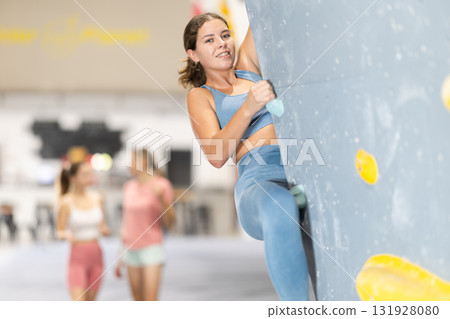 Girl climbs artificial wall bouldering, working out in gym Girl climbs artificial wall bouldering, working out in gym 131928080