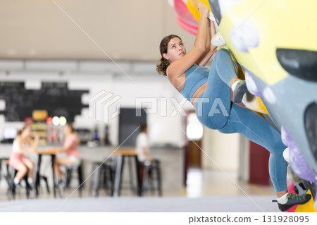 Girl climbs artificial wall bouldering, working out in gym Girl climbs artificial wall bouldering, working out in gym 131928095