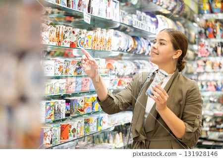 Woman tourist choosing souvenirs while traveling in Spain, looking at handcrafted souvenirs displayed in artisan store 131928146
