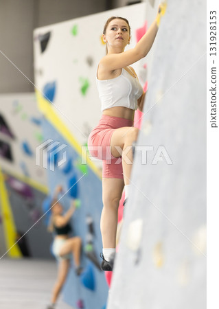 Girl climbs artificial wall bouldering, working out in gym Girl climbs artificial wall bouldering, working out in gym 131928153