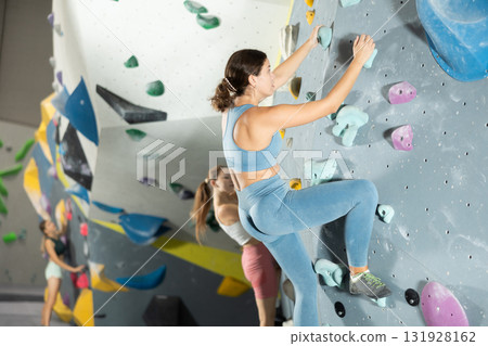 Girl climbs artificial wall bouldering, working out in gym Girl climbs artificial wall bouldering, working out in gym 131928162