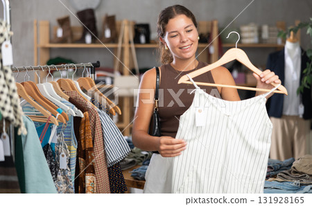 Girl customer choose crop top in store, and buyer carefully examines product. Girl customer choose crop top in store, and buyer carefully examines product. 131928165