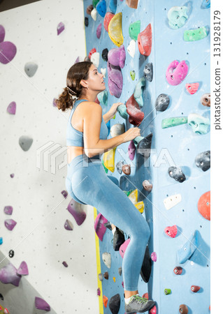 Girl climbs artificial wall bouldering, working out in gym 131928179