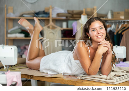 Young fashion designer lying on worktable barefoot in studio Young fashion designer lying on worktable barefoot in studio 131928210