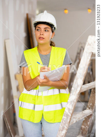 Woman foreman in a protective helmet and yellow vest checks the completed construction work on drawing Woman foreman in a protective helmet and yellow vest checks the completed construction work on drawing 131928233