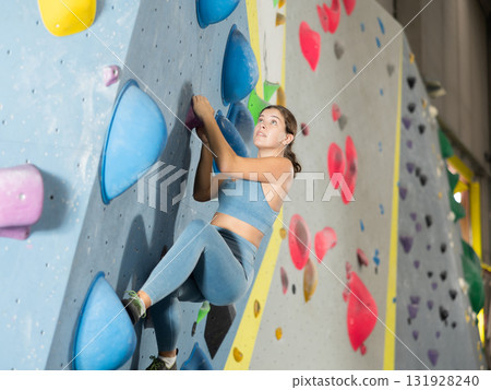 Girl in sportswear practicing rock climbing on climbing wall 131928240