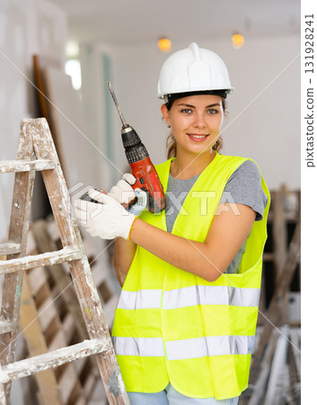 Female foreman in protective yellow vest and hard hat with screwdriver in hand 131928241