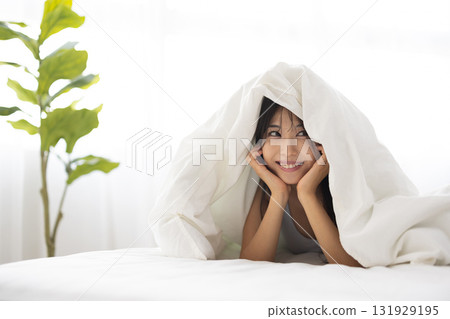 A young woman smiling while covering herself with a futon in the morning sun A young woman smiling while covering herself with a futon in the morning sun 131929195
