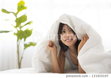 A young woman smiling while covering herself with a futon in the morning sun 131929197