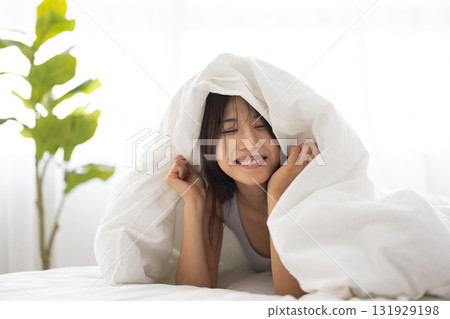 A young woman smiling while covering herself with a futon in the morning sun 131929198