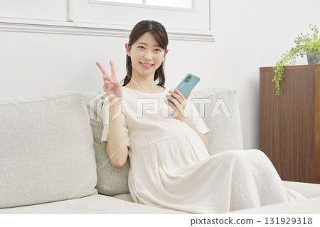 Pregnant woman with smartphone, peace sign, living room 131929318