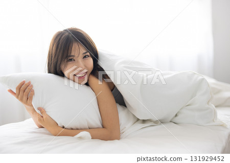 一位年輕女子在清晨的陽光下抱著枕頭微笑 131929452