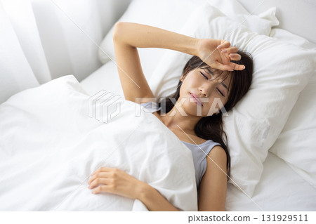 A young woman in bed with a painful expression A young woman in bed with a painful expression 131929511