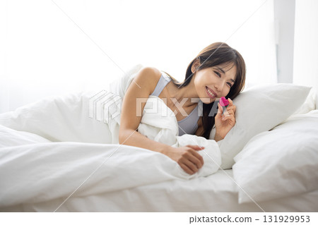 Smiling young woman holding a heart-shaped object in bed 131929953