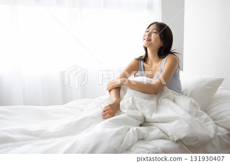 Smiling young woman sitting up in bed Smiling young woman sitting up in bed 131930407