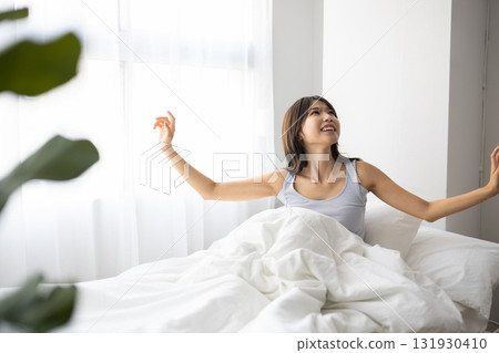 Smiling young woman sitting up in bed 131930410