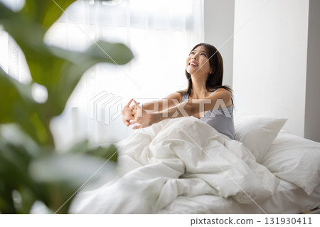 A young woman stretching in bed in the morning sun 131930411