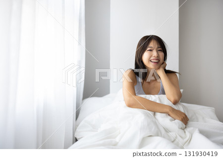 Smiling young woman sitting up in bed Smiling young woman sitting up in bed 131930419