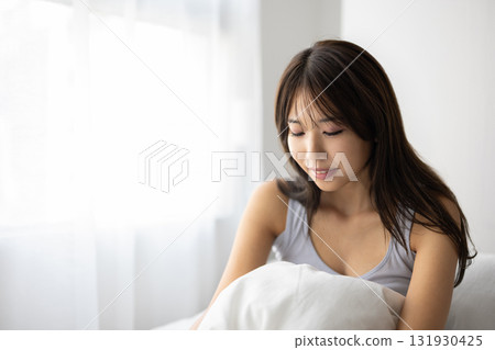 Smiling young woman sitting up in bed Smiling young woman sitting up in bed 131930425